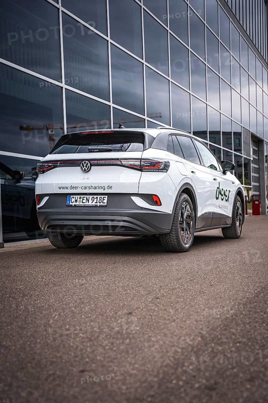White car in front of glass façade on paved road, VW ID4 electric car, Deer Carsharing, Calw, Germany