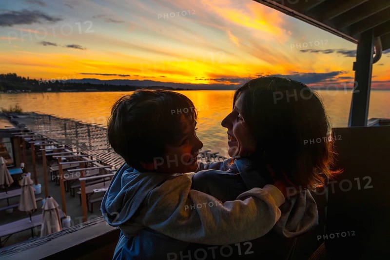Mother and son embracing warmly while enjoying a breathtaking sunset over the serene waters of qualicum beach on vancouver island during summer vacation