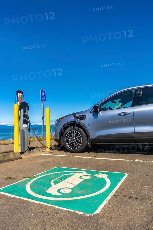 Modern electric car charging at a seaside station on a bright sunny day, highlighting the importance of sustainable transportation and the benefits of clean energy solutions