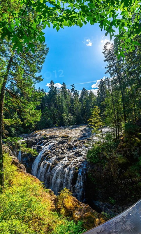 Cascading over rocks, englishman river falls creates a stunning spectacle amidst a vibrant green forest under a bright blue sky on vancouver island, british columbia