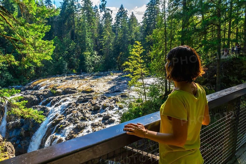 Tourist wearing a yellow t shirt is enjoying the view of englishman river falls from a viewpoint on vancouver island, british columbia, canada, during a sunny summer day