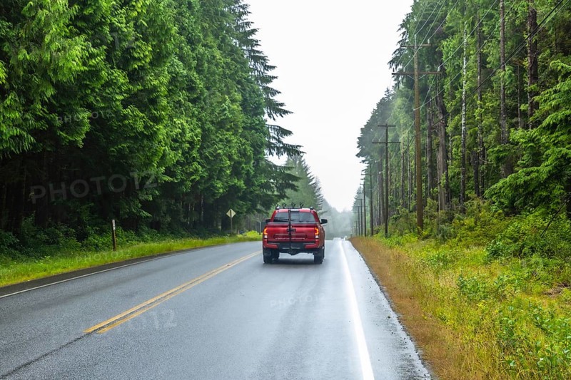 Red pickup truck driving away on a scenic rainforest road during a cloudy day in ucluelet, a small district municipality on the west coast of vancouver island in british columbia, canada