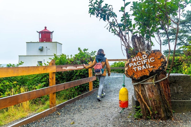 Female tourist walking along the gravel path of the wild pacific trail near amphitrite point lighthouse in ucluelet, british columbia, surrounded by lush greenery