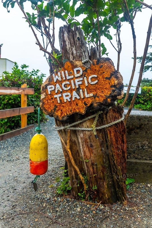 Rusty sign marking the wild pacific trail in ucluelet, british columbia, featuring a weathered wooden post, nautical rope, and a hanging buoy