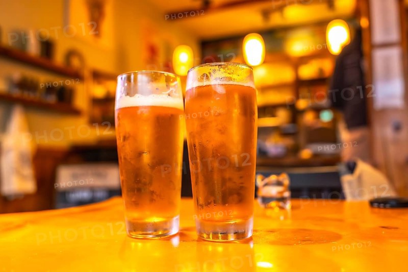 Two glasses of cold craft beer sit on a wooden table in a cozy pub in ucluelet, british columbia, with a blurred background hinting at the lively atmosphere