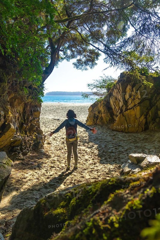 Female tourist with open arms enjoying breathtaking view of mackenzie beach after hiking through lush rainforest trail in tofino, vancouver island, british columbia, canada