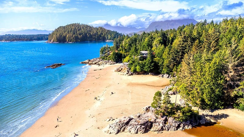 Turquoise water gently caressing the sandy shores of mackenzie beach, surrounded by lush green forest and rocky outcrops, creates a breathtaking coastal panorama in tofino, vancouver island