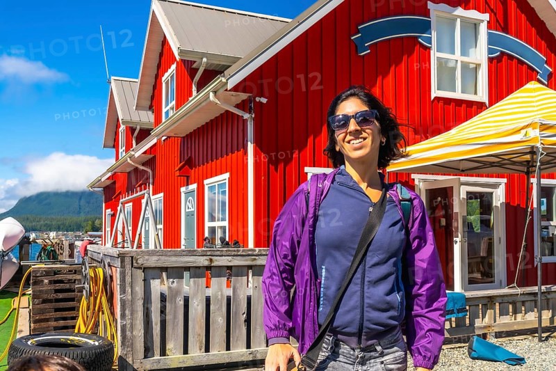 Happy tourist smiling in front of a characteristic red building in tofino, a popular travel destination on vancouver island, british columbia, canada, during a sunny summer day
