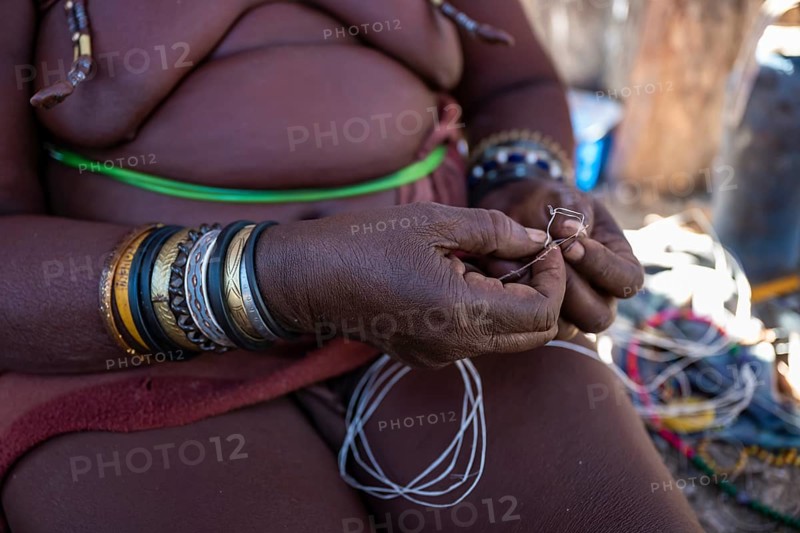 Himba woman doing handiwork, making hand bands for tourists, traditional Himba village, Kaokoveld, Kunene, Namibia