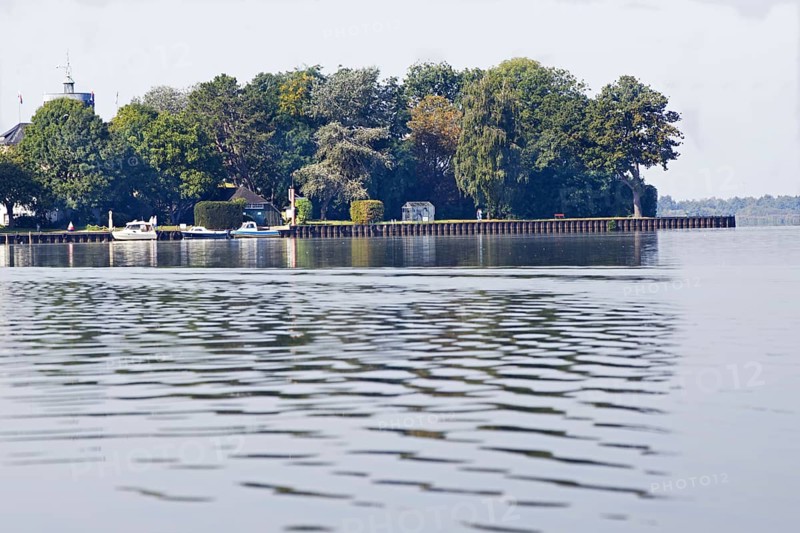 Tranquil landscape (Wilhelmstein Island) on the lakeshore with a dense row of trees and boats on slightly rippled water, Steinhude, Steinhuder Meer