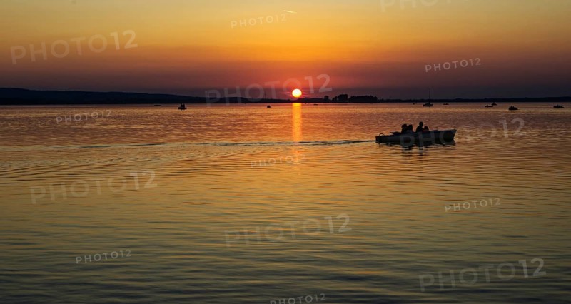 Boat over calm waters at sunset, orange dusk, Steinhude Steinhuder Meer