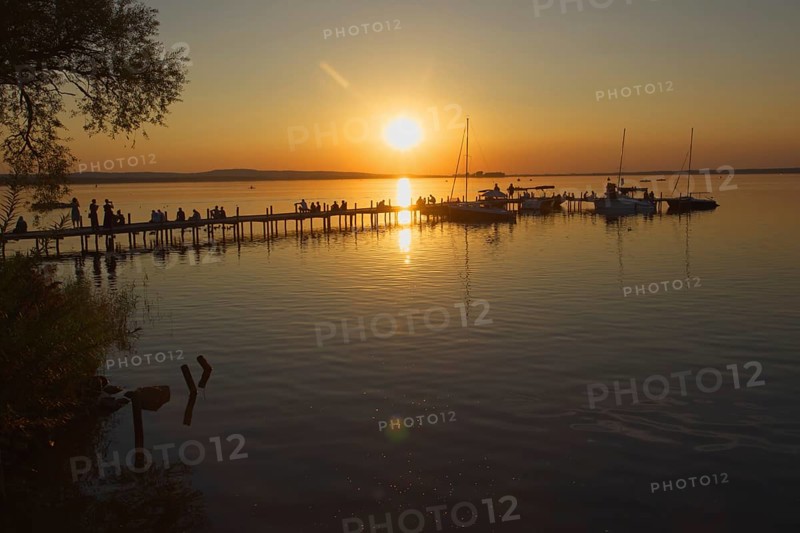 Sunset on Lake Steinhude with people on a jetty and sailboats, relaxed atmosphere, Steinhude