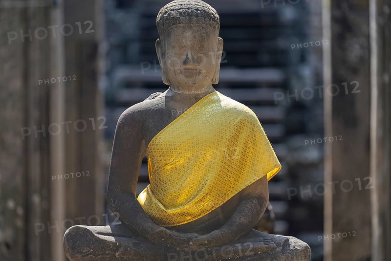 Sandstone Buddha statue, (Dhyana-mudra: gesture of meditation), with yellow tunic, on the north side of the Bayon Temple, with huge stone-carved faces of the Bodhisattva Lokeshvara, also known as Avalokiteshvara, Angkor Thom, UNESCO World Heritage Site, Angkor Wat, Siem Reap, Cambodia