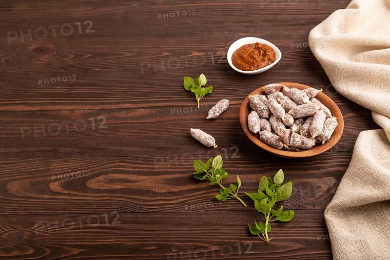 Small smoked Chicken sausages in wooden bowl on brown wooden background and linen textile. side view, copy space