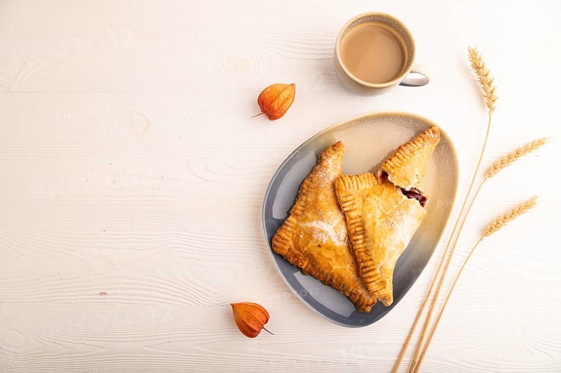 Triangles Pie, Puff Pastry, Samsa with cherry jam on white wooden background, cup of coffee, top view, flat lay, copy space