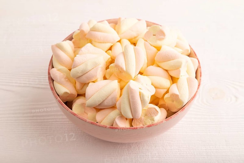Orange and pink marshmallow in ceramic bowl on white wooden background, side view, copy space, minimalism