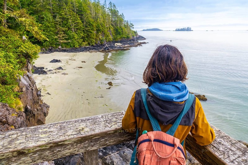 Tourist with a backpack is enjoying a breathtaking view of the ocean and coastline from a wooden viewpoint in tofino, a popular destination on vancouver island, british columbia, canada