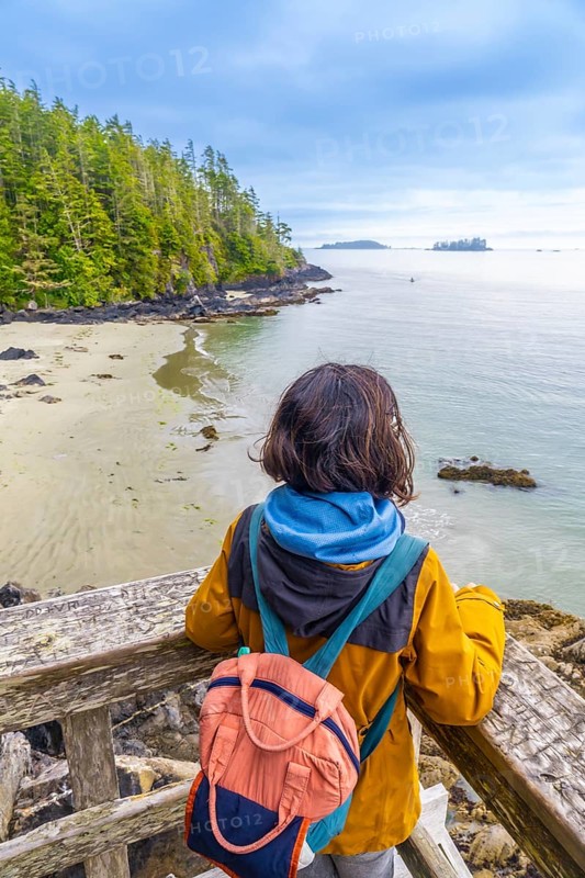 Tourist with a backpack is enjoying a breathtaking view of the ocean and coastline from a wooden viewpoint in tofino, located on vancouver island, canada