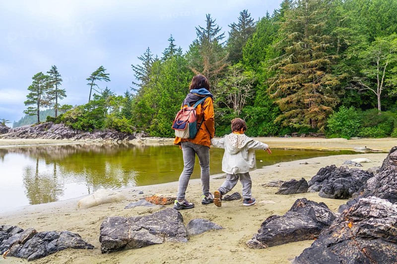 Mother and son walking along the shore of mackenzie beach in tofino, enjoying the breathtaking natural beauty of vancouver island on a cloudy summer day