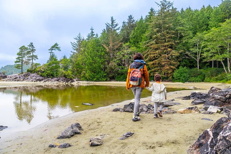 Mother and daughter, hand in hand, enjoy a peaceful stroll along mackenzie beach in tofino, british columbia, surrounded by the serene beauty of vancouver island's lush rainforest and calm waters