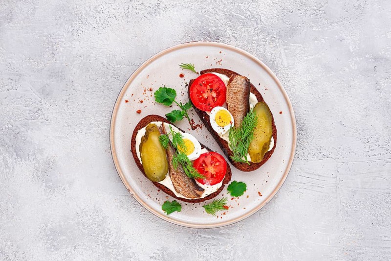 Sandwiches on rye bread, with sprats, quail eggs, fresh tomatoes and pickled cucumber, appetizer, breakfast, homemade