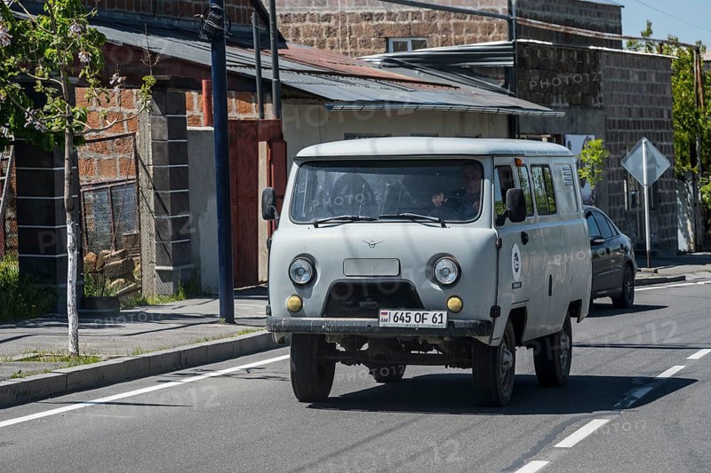 White pickup truck drives past old buildings on a quiet street, UAZ Buchanka, Armenia