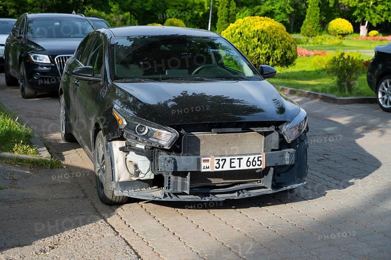 Black Kia parked in a green parking environment with front damage, Armenia