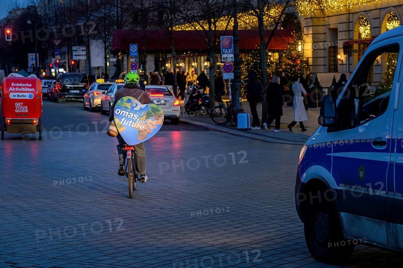 Grandma for Future is cycling back after the Fridays for Future rally. On the left, bicycle rickshaw with the inscription: Discover activities in Berlin, on the right, police personnel carrier. Berlin, 12.12.2025