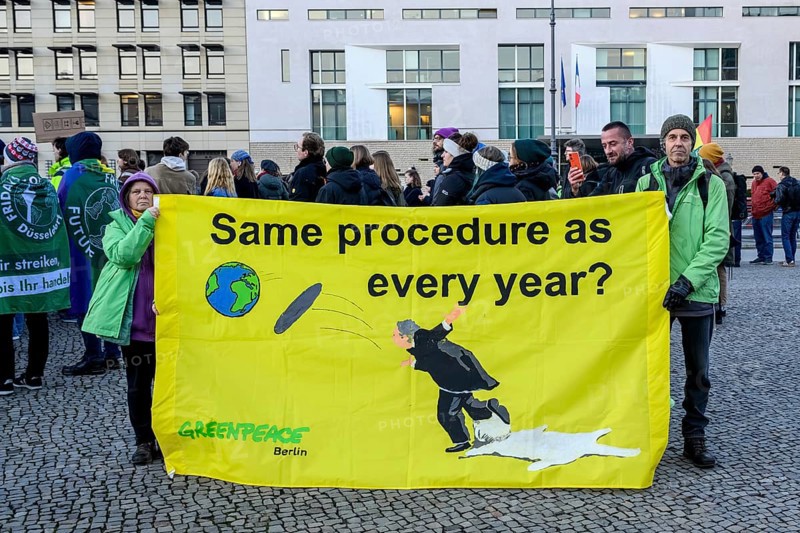 Greenpeace activists at Fridays for Future rally on 10 years of Paris Agreement and 7 years of Fridays for Future. Transparent: Same procedure as every year? with soil falling from a tray and a stumbling butler. Pariser Platz, Berlin, 12.12.2025