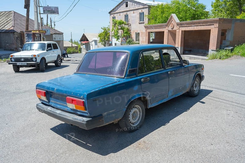 A blue car at an urban intersection on a clear sunny day, Lada 2107, also WAS-2107, VAZ-2107, Lada Nova or Lada Riva drives without a license plate, Armenia