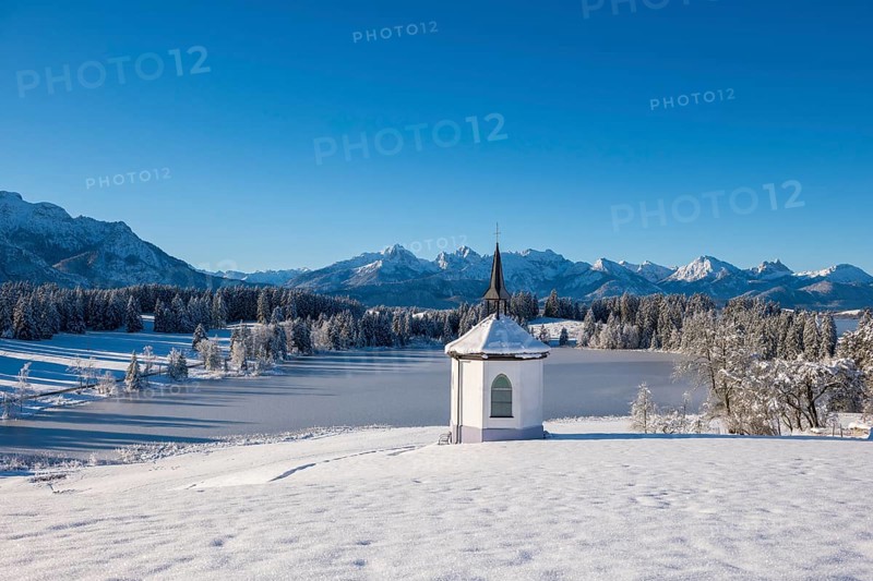 Snowy landscape with chapel and mountains in the background under clear blue sky, Hegratsrieder See, near Füssen, Ostallgäu, Allgäu, Bavaria, Germany