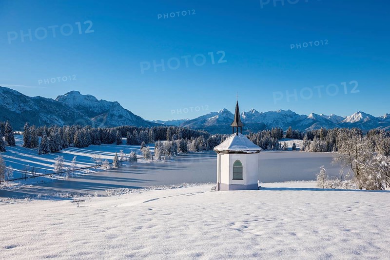 Small chapel in front of snow-covered mountains and forests under a clear sky, Hegratsrieder See, near Füssen, Ostallgäu, Allgäu, Bavaria, Germany