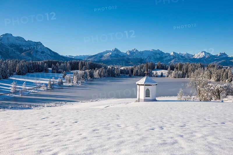 Snow-covered plain with a chapel and mountains under bright blue sky, Hegratsrieder See, near Füssen, Ostallgäu, Allgäu, Bavaria, Germany