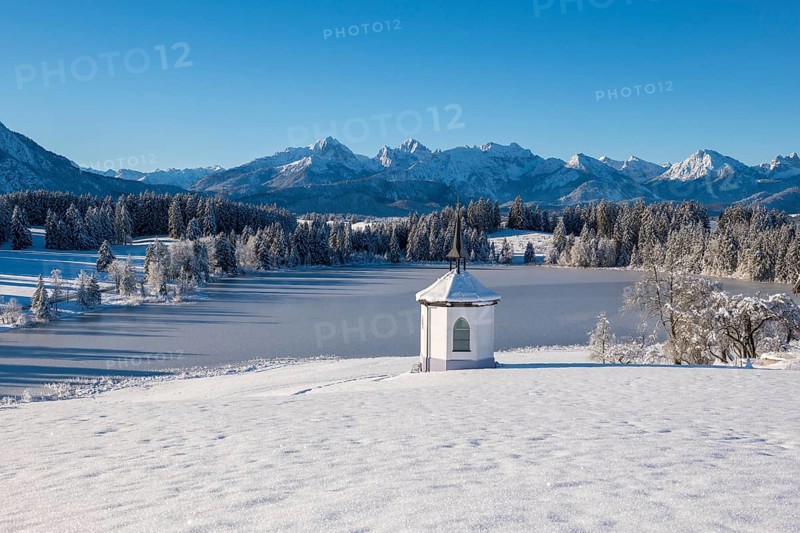 Landscape with snowy chapel on the shore of a frozen lake in front of Bergen, Hegratsrieder See, near Füssen, Ostallgäu, Allgäu, Bavaria, Germany