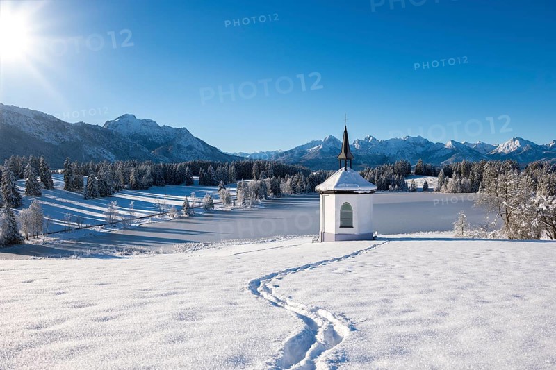 Chapel in snow with footprints and sunny mountain landscape, Hegratsrieder See, near Füssen, Ostallgäu, Allgäu, Bavaria, Germany