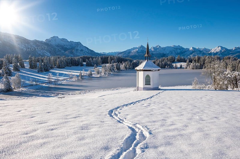 Snowy landscape with chapel and footprints, surrounded by mountains and forests, Hegratsrieder See, near Füssen, Ostallgäu, Allgäu, Bavaria, Germany