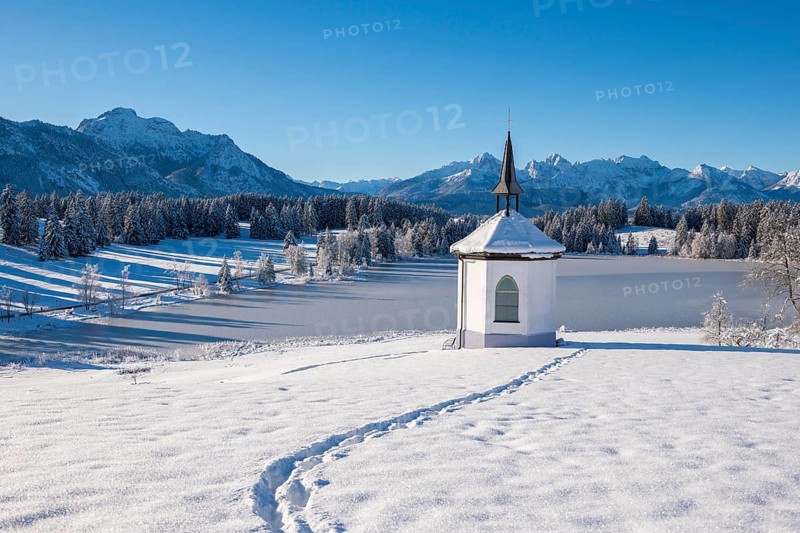 Snowy landscape with chapel and footprints against a mountain backdrop, Hegratsrieder See, near Füssen, Ostallgäu, Allgäu, Bavaria, Germany