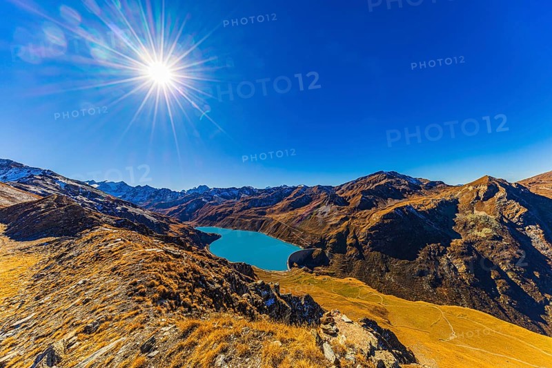 The sun shines over the mountains of the Val d'Anniviers, below the dam and the turquoise Lac de Moiry reservoir, Valais Alps, Canton of Valais, Switzerland
