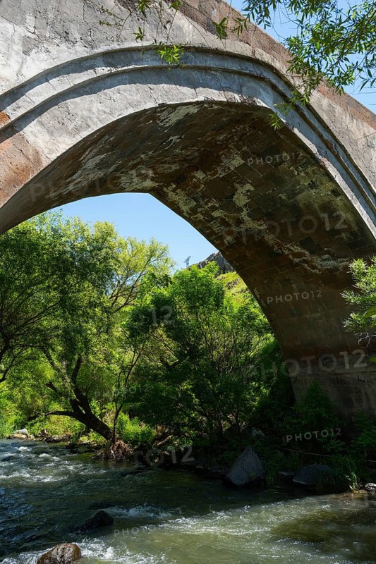 Old stone bridge over a flowing river surrounded by dense nature and trees, part of a three-arched bridge over the Kassagh from 1664, Ashtarak bridge, Ashtarak, Aragazotn province, Armenia