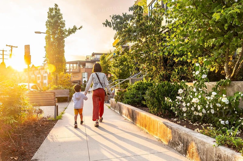 Mother and son are walking hand in hand down a sidewalk in a residential neighborhood of vancouver, british columbia, during a beautiful sunset, enjoying quality time together