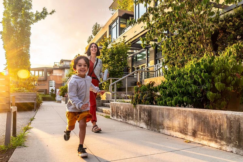 Happy child running joyfully on the sidewalk in vancouver, british columbia, canada, with mother walking closely behind during a beautiful sunset near their home