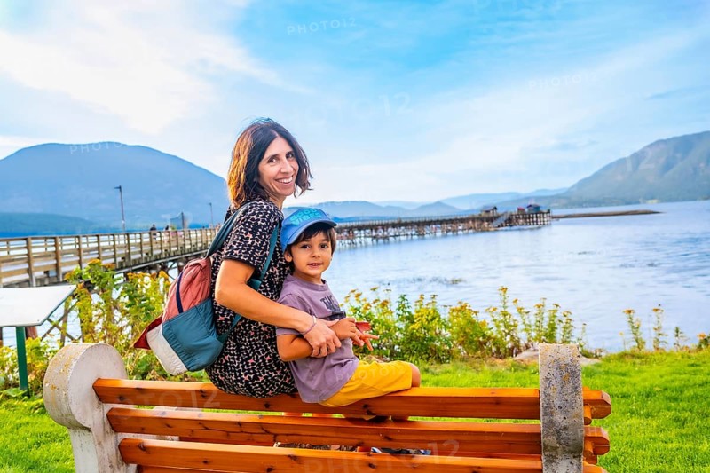 Mother and her son are sitting on a wooden bench, enjoying the scenic view of the salmon arm wharf and the shuswap lake in british columbia, canada, on a beautiful summer day