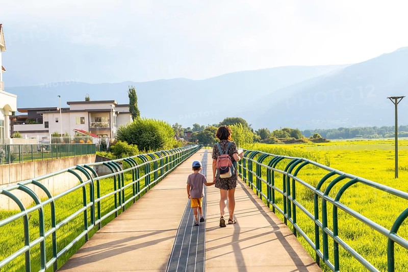 Mother and son enjoying a leisurely stroll on a pedestrian bridge, surrounded by lush greenery and mountains in the picturesque city of salmon arm, british columbia, canada