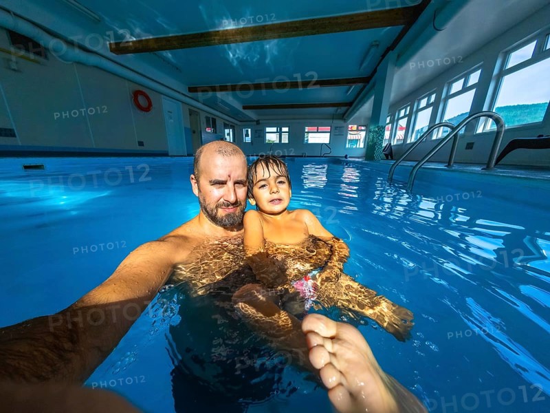 Father and son are taking a selfie while having fun and enjoying time together in a swimming pool during their vacation, creating a cherished memory