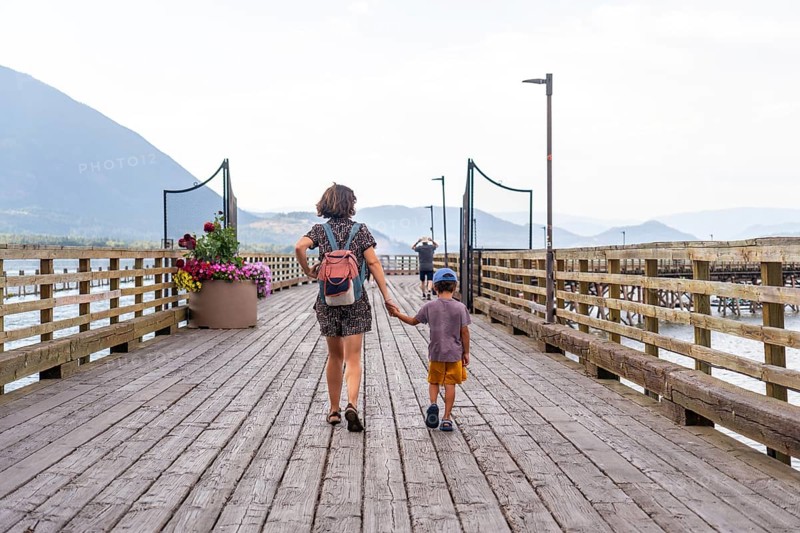 Mother and son walking hand in hand along a scenic wooden pier, surrounded by serene waters and majestic mountains in salmon arm, british columbia, embracing family bonding in nature