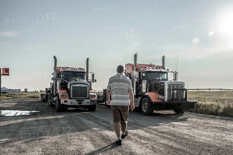 Trucker walking towards two semi trucks parked on a gravel road near hemlock grove boardwalk in the canadian rockies, showcasing a scene of transportation and logistics
