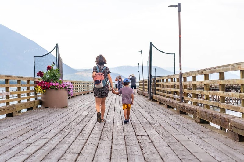 Mother and son enjoying a leisurely stroll along a picturesque wooden pier in salmon arm, british columbia, surrounded by stunning natural beauty and a tranquil atmosphere