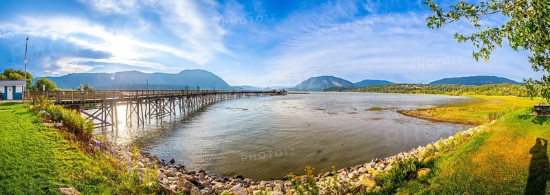 Panoramic view of a long wooden pier stretching into the tranquil waters of shuswap lake, surrounded by the scenic beauty of salmon arm, british columbia, on a sunny day