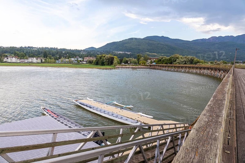 Dragon boats are tied up at a floating dock near a wooden pier, with the city of salmon arm and the shuswap mountains in the background on a cloudy summer day in british columbia, canada
