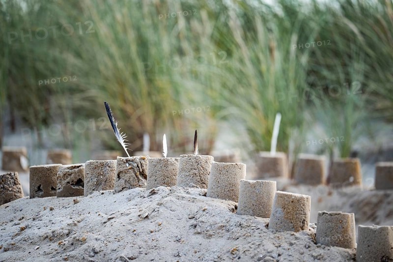 Sandcastle on the beach, detailed view of a sand castle with small towers and dug in the sand, behind it dunes with beach grass in a soft background, diffuse daylight and quiet, playful coastal atmosphere, Schillig, Lower Saxony, Germany